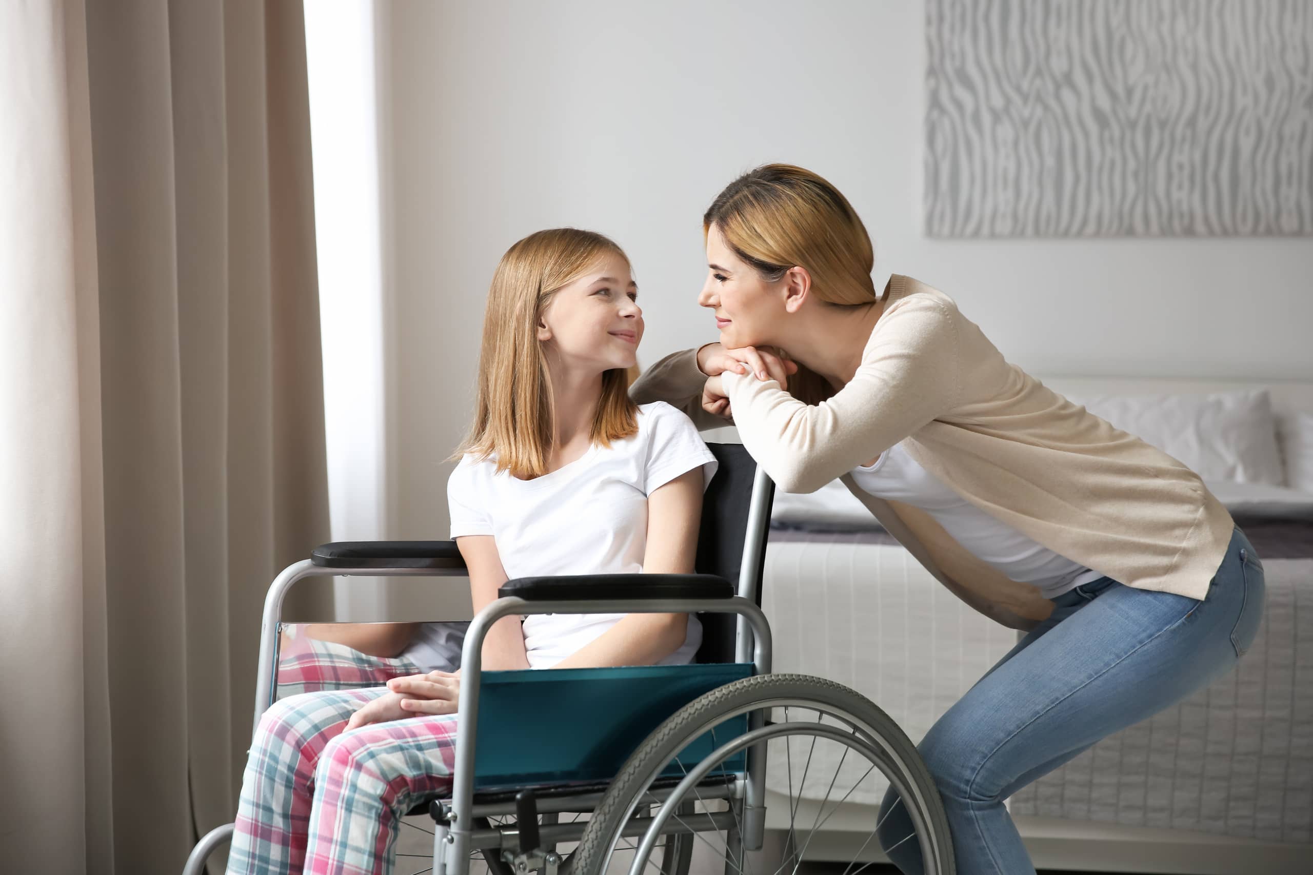 Maminka se sklání k dceři na invalidním vozíku